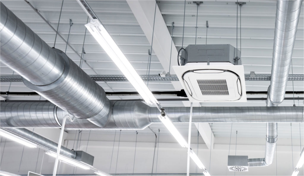 Réseau de ventilation et unité de climatisation installés au plafond d’un bâtiment tertiaire. Le suivi des équipements CVC permet de visualiser leur fonctionnement, de détecter les dérives plus rapidement et d’optimiser les performances énergétiques tout en préservant le confort des occupants.