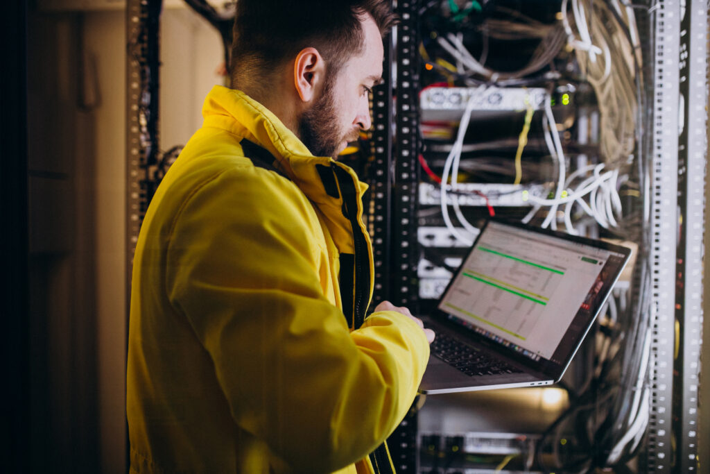 A technician who works on computer racks and technical equipment, using a laptop to monitor, diagnose, or adjust the building's connected systems in real time.