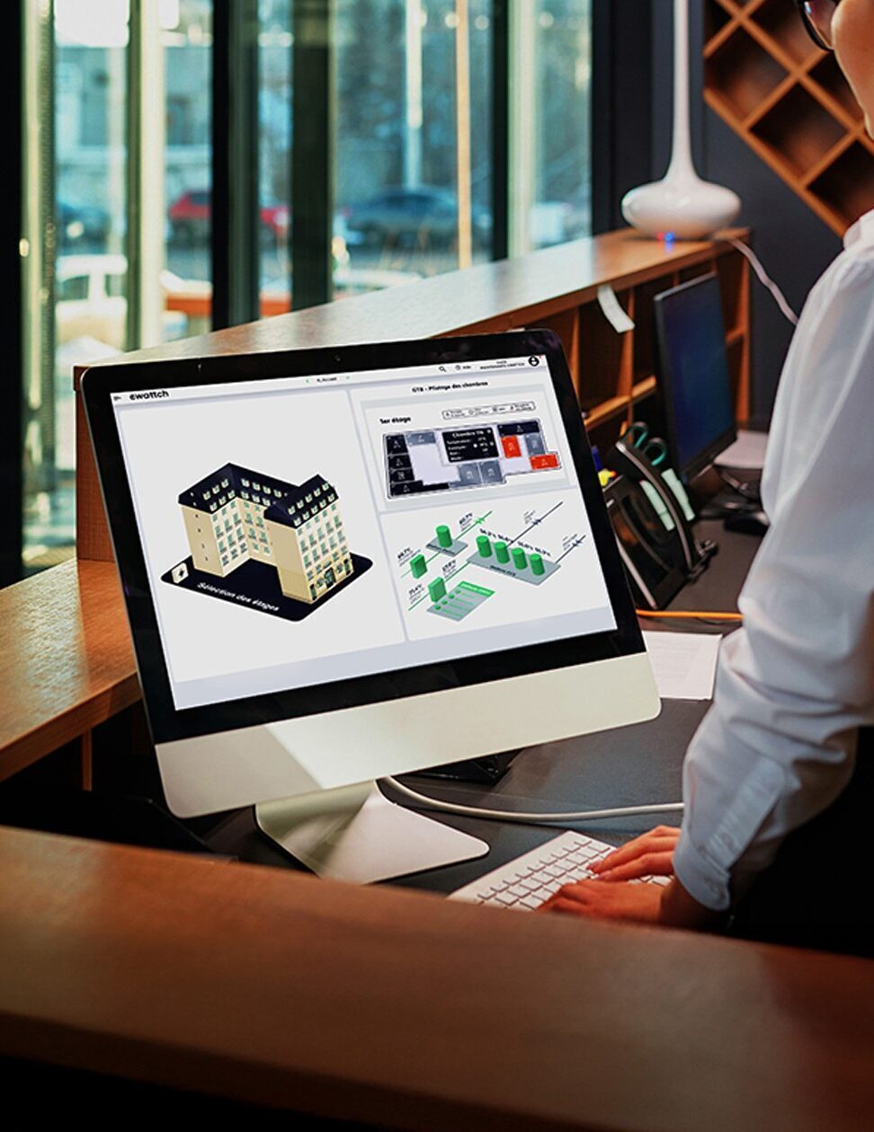 Employé d’hôtel utilisant un ordinateur avec la plateforme EwattchCloud pour superviser les chambres et la consommation énergétique.