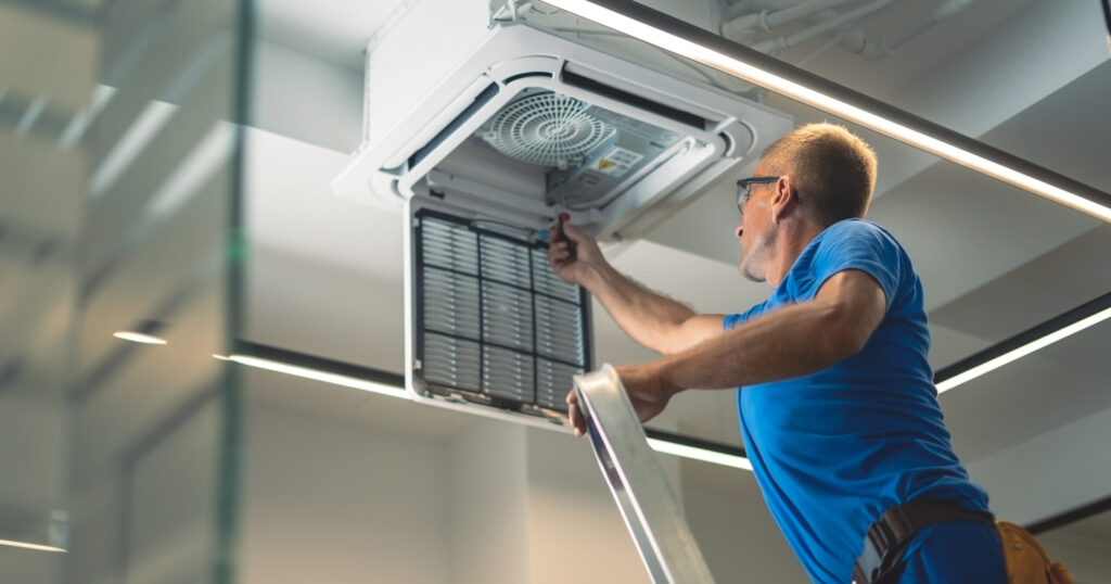 Technicien réalisant la maintenance d’un climatiseur en plafond dans un bâtiment tertiaire, lors d’une intervention HVAC pour assurer la performance et la fiabilité des installations.