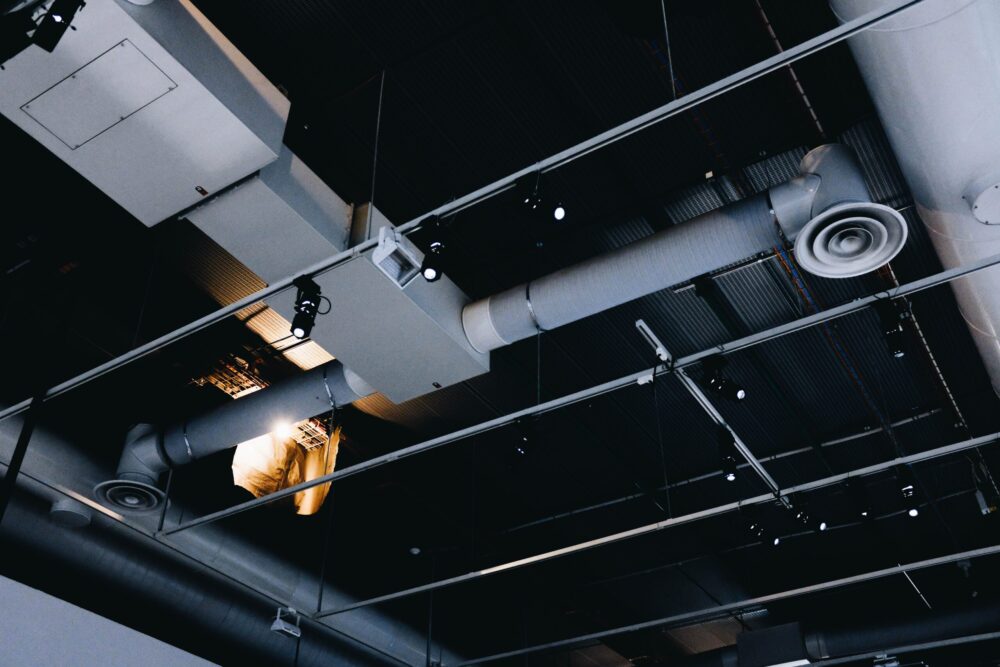 A low-angle shot of a black metal ceiling with white ventilation pipes