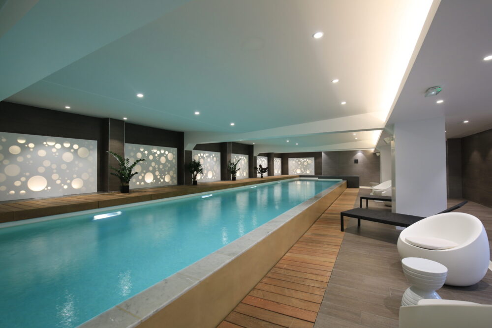 Piscine intérieure moderne dans un hôtel avec espace détente et éclairage tamisé.