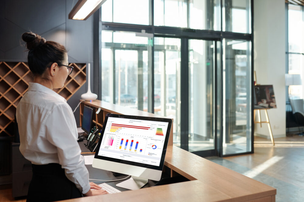A front desk clerk checking an energy dashboard in a hotel lobby.