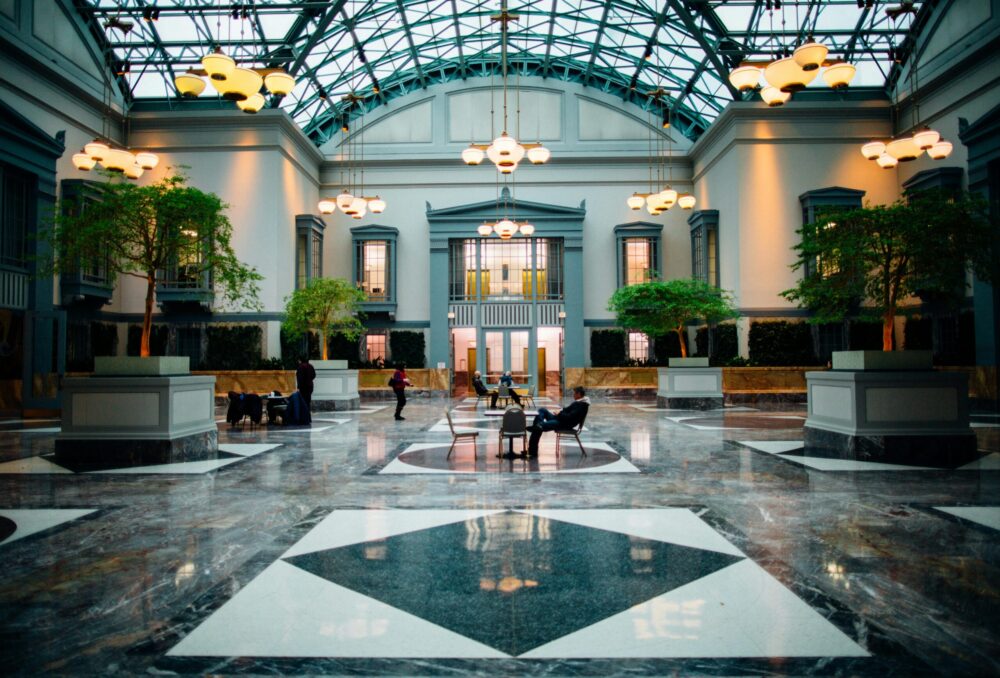 A spacious hotel lobby with a glass roof, marble flooring, and an elegant reception area.