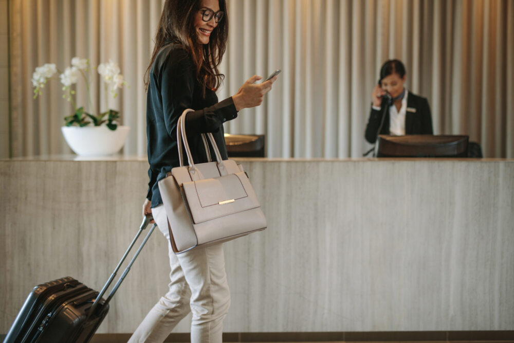 Cliente avec valise utilisant son téléphone dans le hall d’un hôtel haut de gamme.