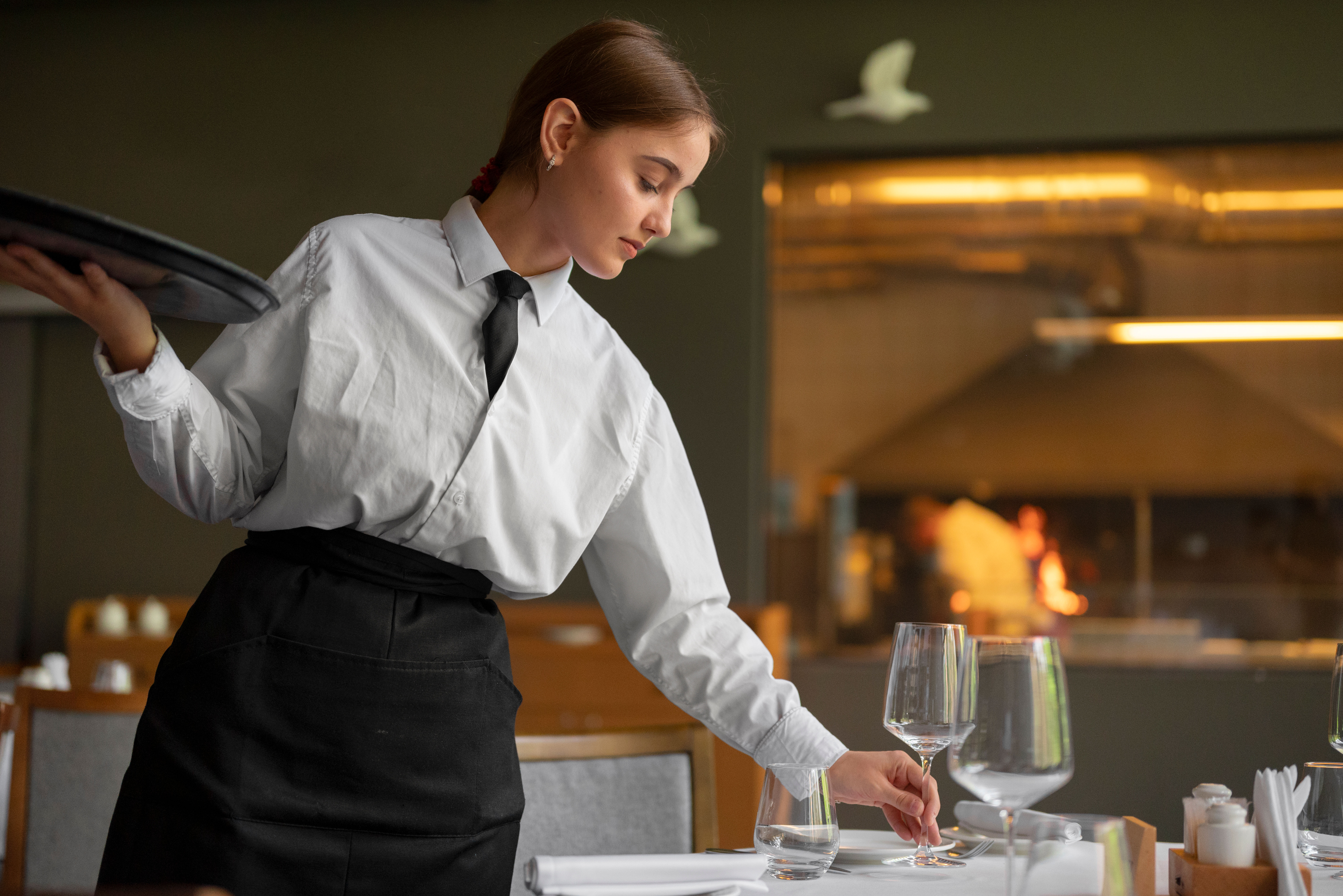 A waitress setting a table in a hotel restaurant with an ambiance and attentive service.