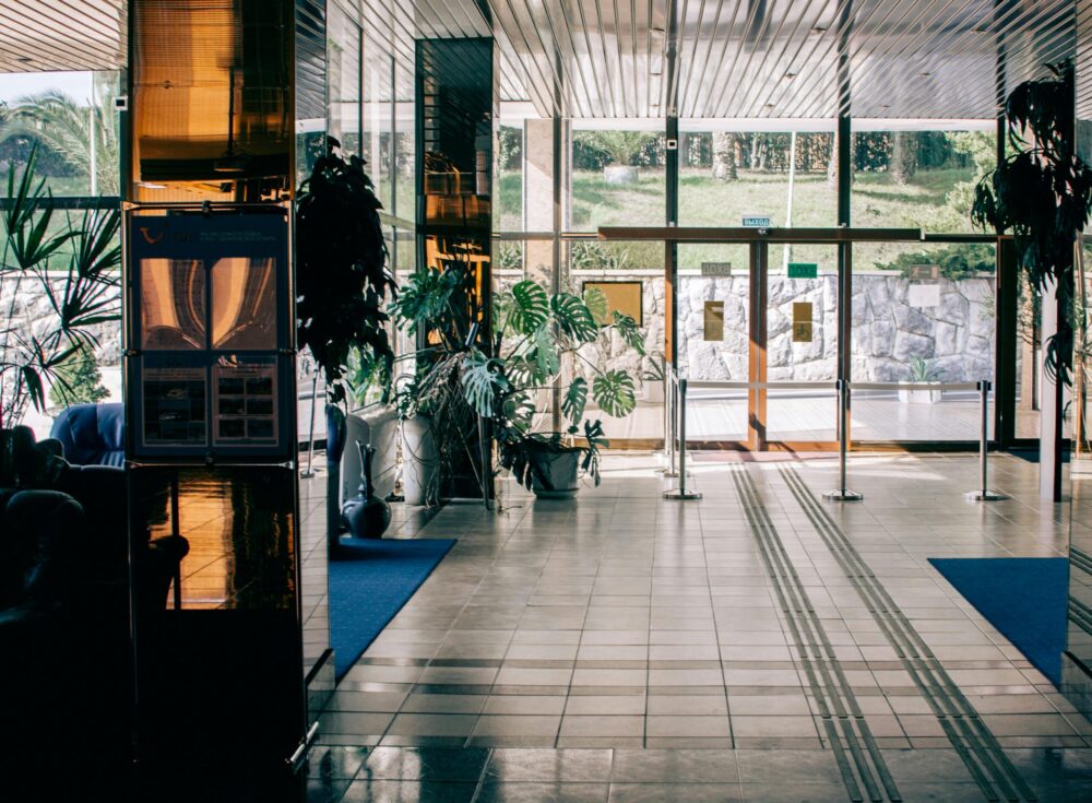 Hall d’entrée moderne avec grandes baies vitrées, plantes et espaces d’accueil dans un hôtel.