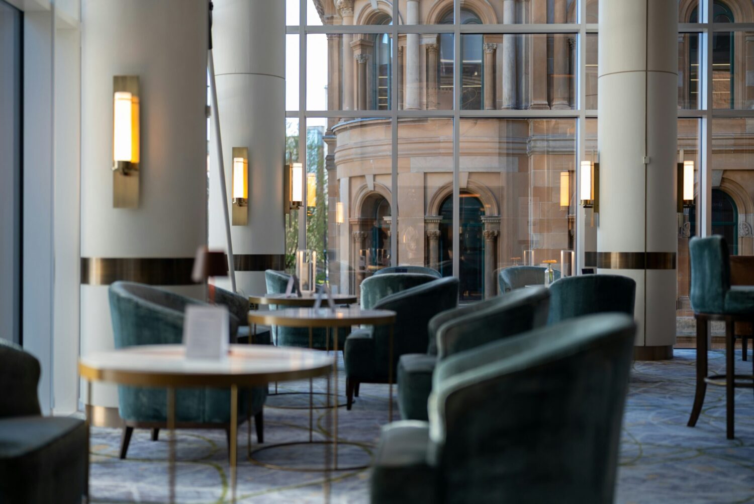 Salon d’hôtel avec fauteuils confortables, tables basses et grandes baies vitrées donnant sur l’extérieur.