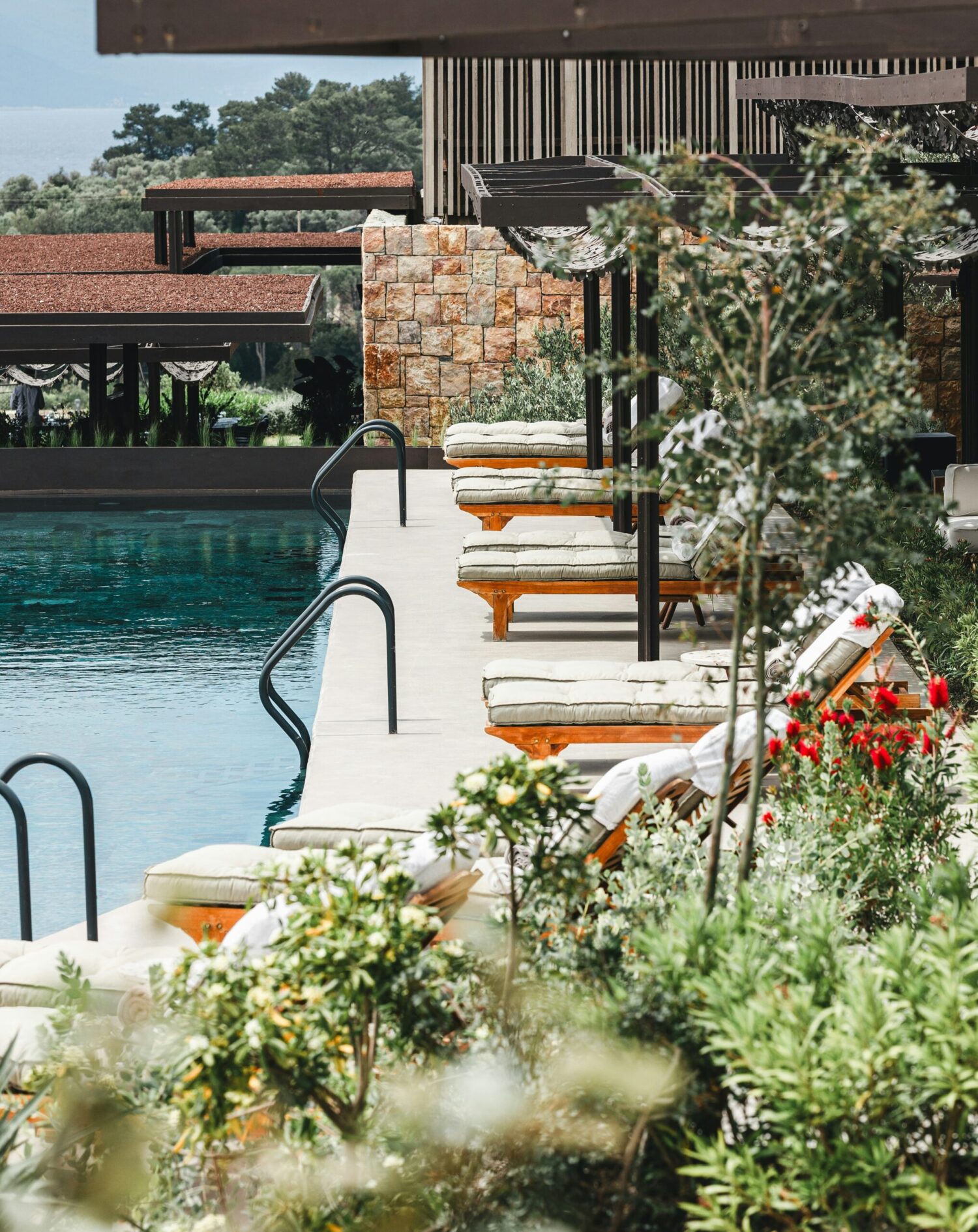 An outdoor hotel pool with lounge chairs, landscaped greenery, and a relaxation area.